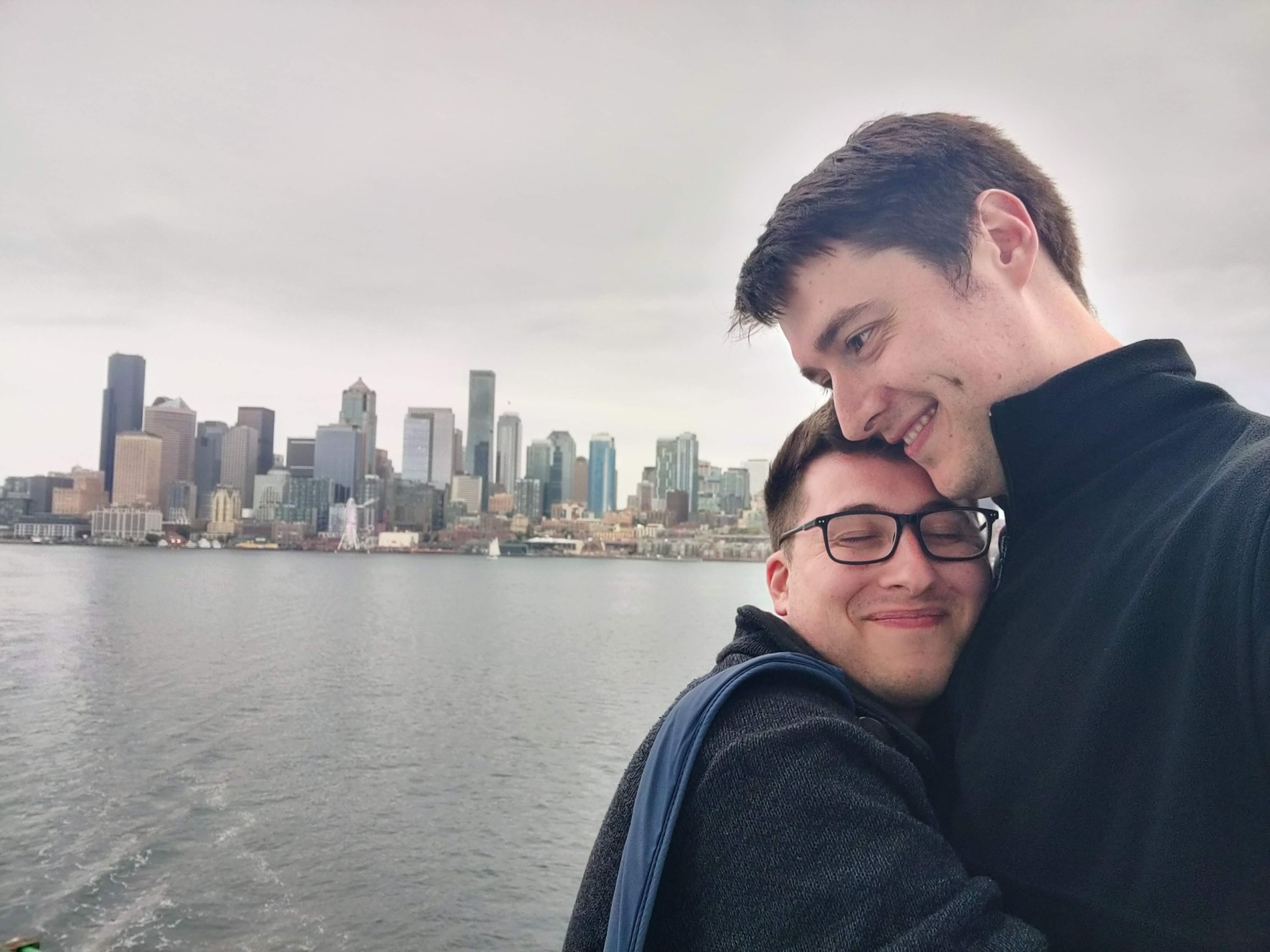 Aaron and Peter embracing with a city skyline across the water